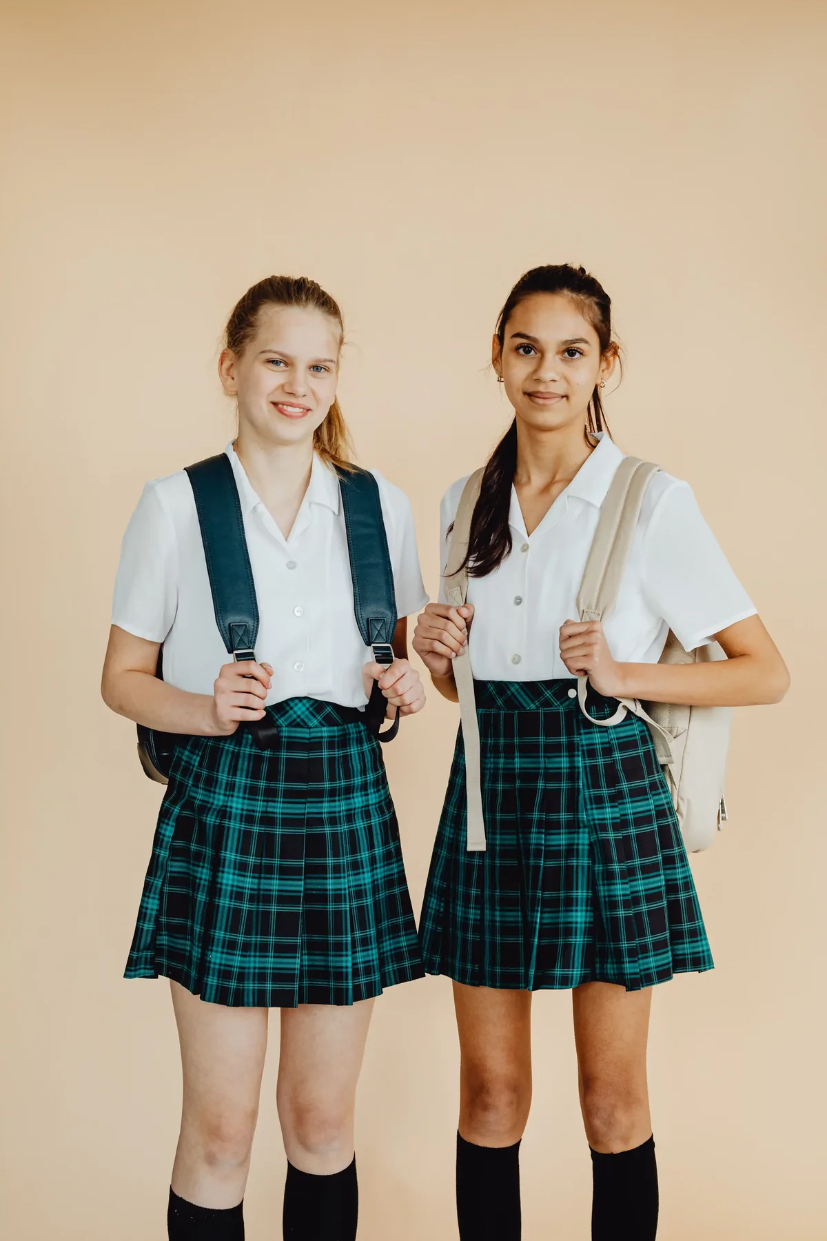 Duas estudantes uniformizadas com camisa branca, saia xadrez e mochila